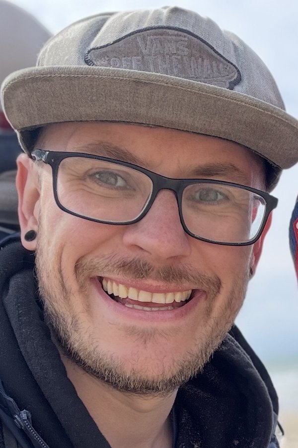 Sam Rowley on a beach, in a cap and glasses
